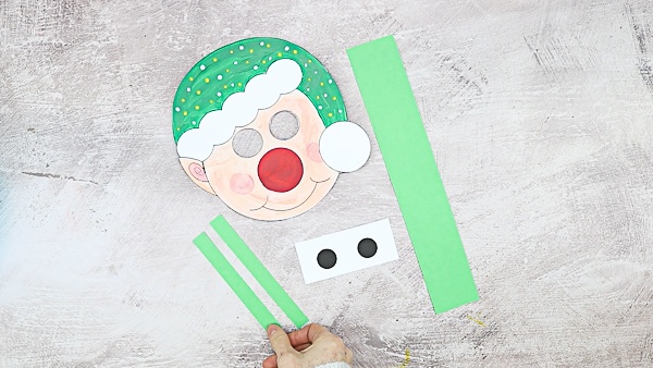 Once the elf template is colored in, cut out the elements and cut out a further three green strips; One strip should be wide and the full length of a piece of A4 card, the remaining two short and slim - log enough to cover the eye holes and support the long strip.