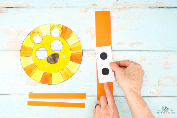 Image showing the eyes being glued to the middle of a long and wide strip of orange cardstock.