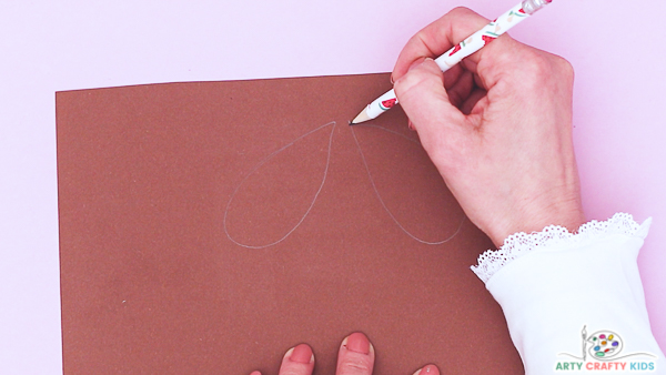 Image showing a hand drawing a pair for large wings onto brown paper.