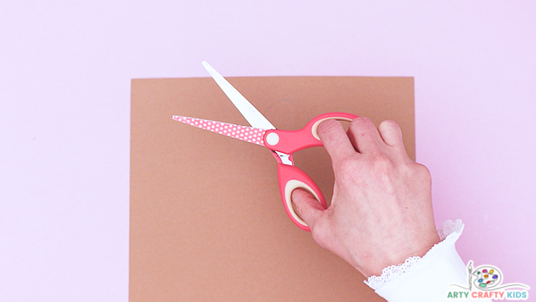 Image showing a hand about the cut a circle out of a sheet of brown paper.