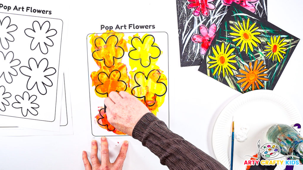 Image of a hand completing the scrape painting process. The flowers are a blend of yellow, orange and red.