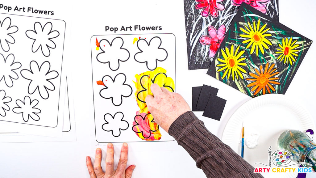 Image of a hand painting the flowers with the scrape painting technique. The paint is yellow, orange and red.