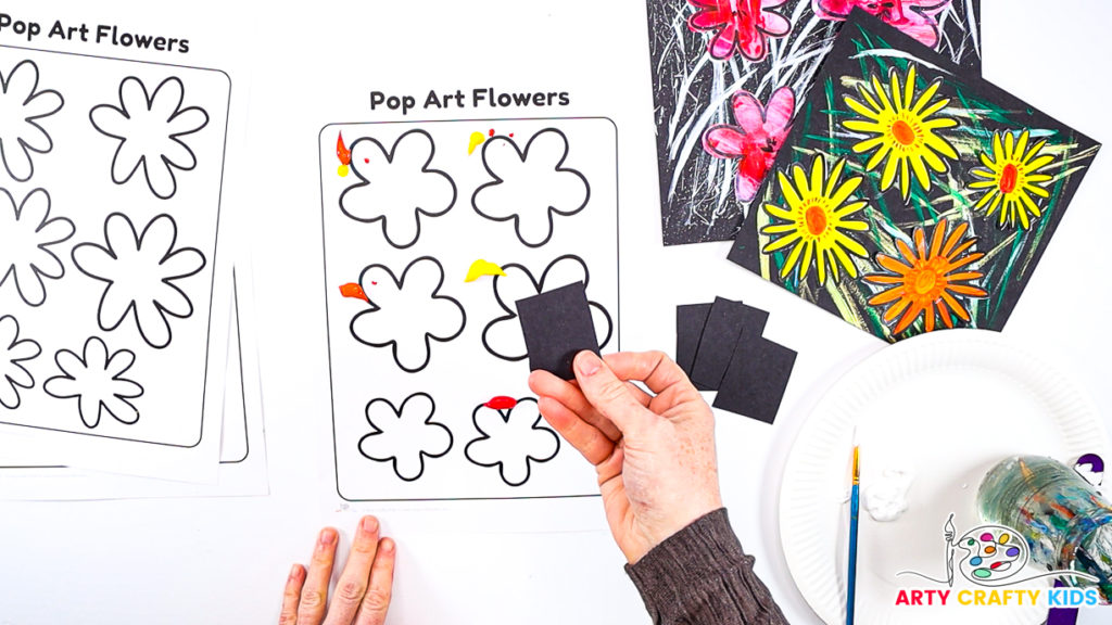 Image of a hand holding a piece of black card stock for painting the flowers with the scrape painting technique.