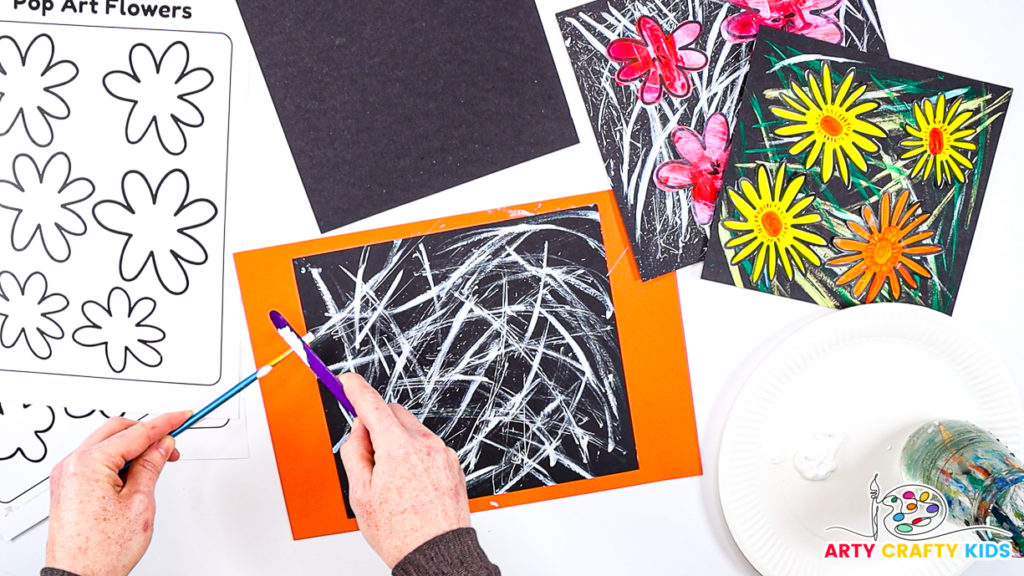 Image of a hand splattering white paint across the square piece of card stock.