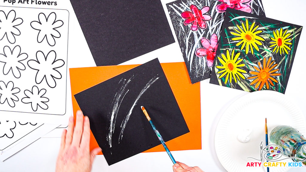 Image of a hand brushing white lines across a square piece of black cardstock .