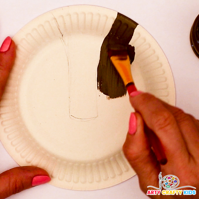 Image of a hand painting a white paper plate brown.