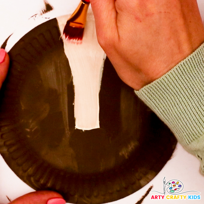 Image of a hand painting a white strip onto the paper plate.
