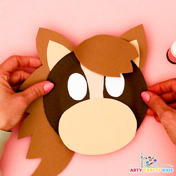 Image of a hand gluing the mane onto the back of the paper plate.
