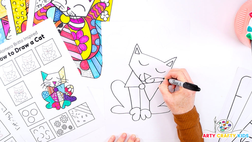 Image of a hand using the how-to-draw step-by-step printable to draw Britto's cat's facial features.