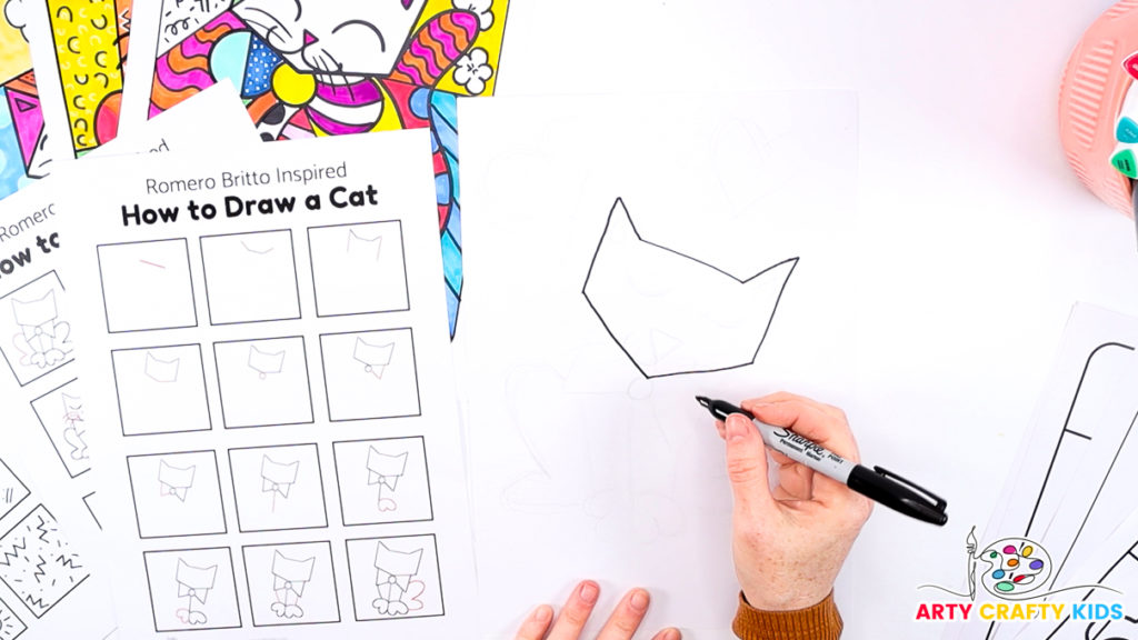 Image of a hand using the how-to-draw step-by-step printable to draw Britto's cat's head.