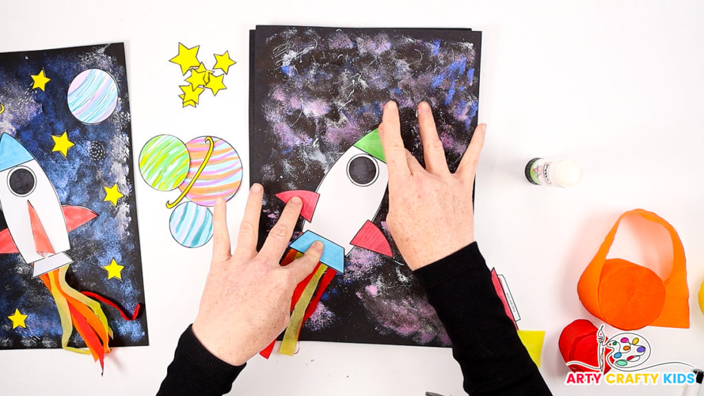 Image of a hand glueing the spaceship onto the galaxy painting.