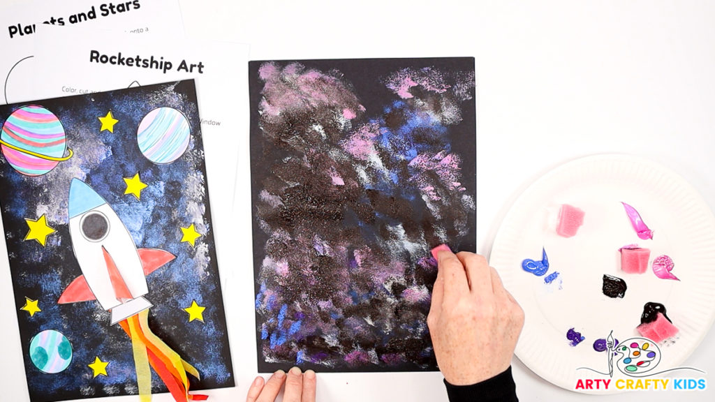 Image of a hand dabbing black paint across the colored to create cosmic constrast.