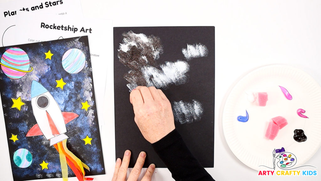 Image of a hand dabbing white paint into a black sheet of cardstock.