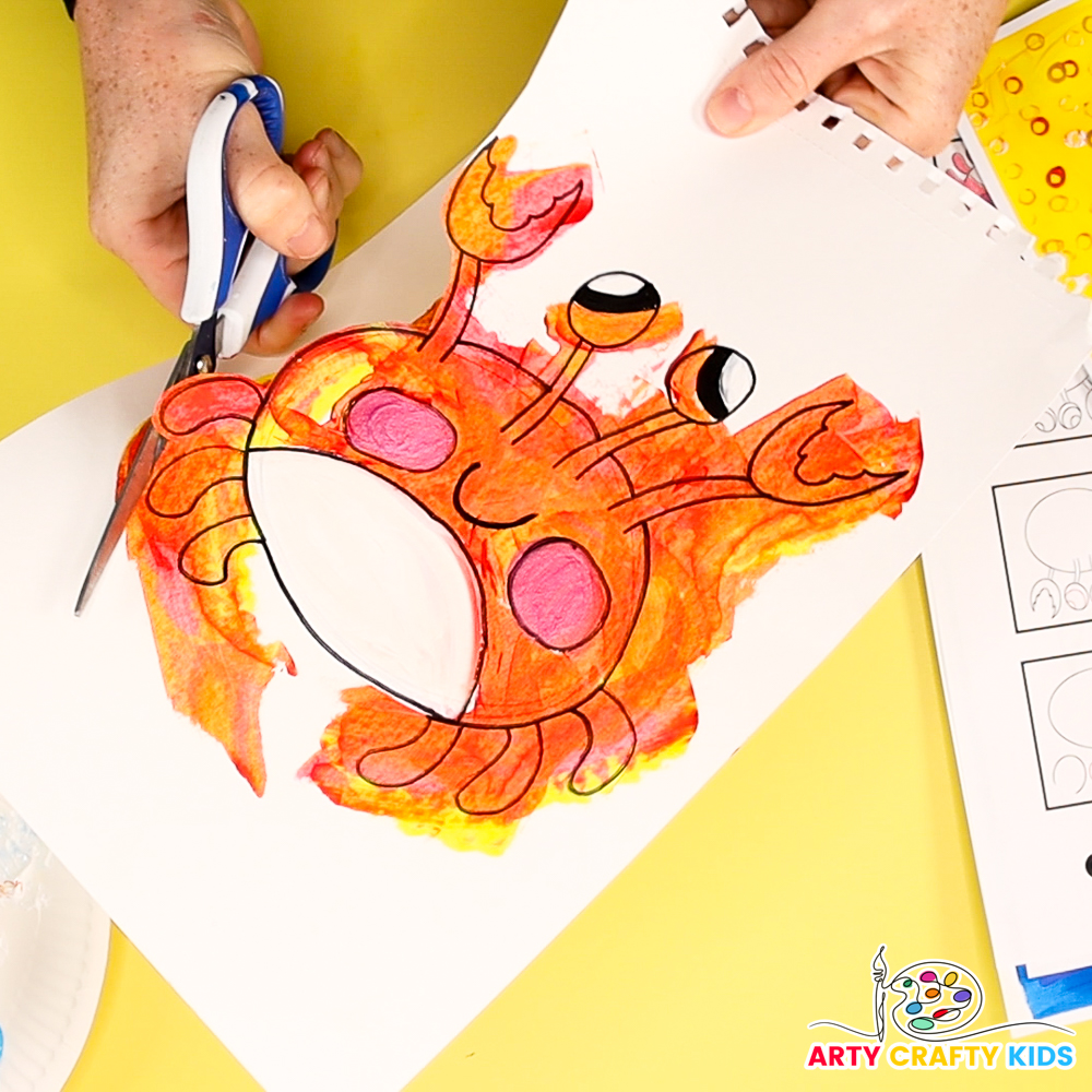 The image shows a hand carefully cutting out the crab drawing.