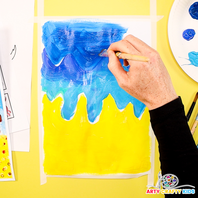 The image shows a hand painting the upper half of a piece of cardstock blue to represent the sea.
