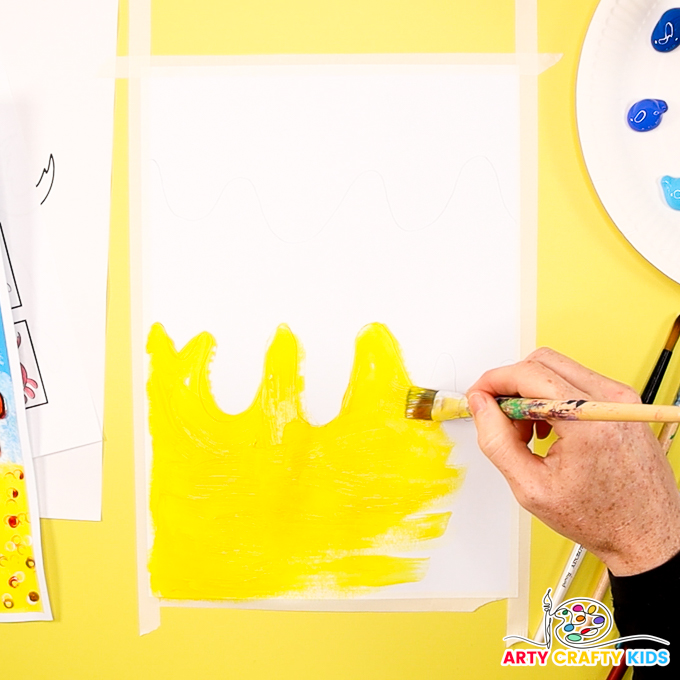 The image shows a hand painting the bottom half of a piece of cardstock yellow to represent sand.