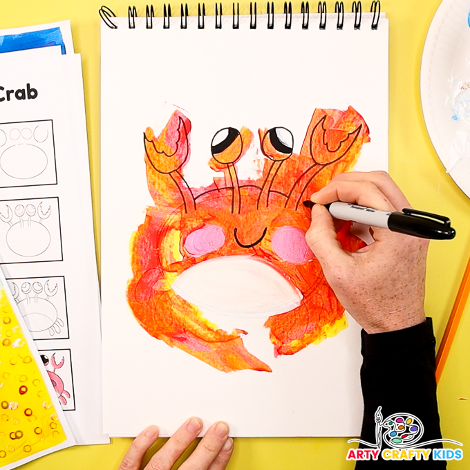 The image shows a hand outlining the crab illustration with a black marker pen.
