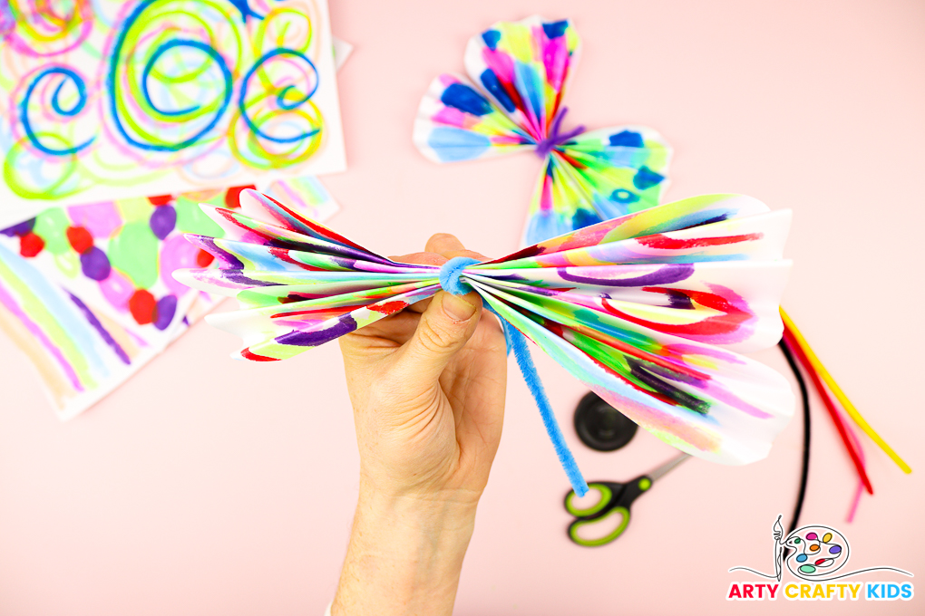 Image of a hand tieing a pipe cleaner around the folded papers.