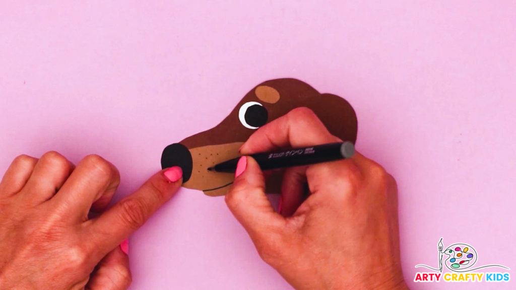 Image of a hand drawing a cute smile onto the dog's muzzle, with the eye, brow, ears and nose affixed.