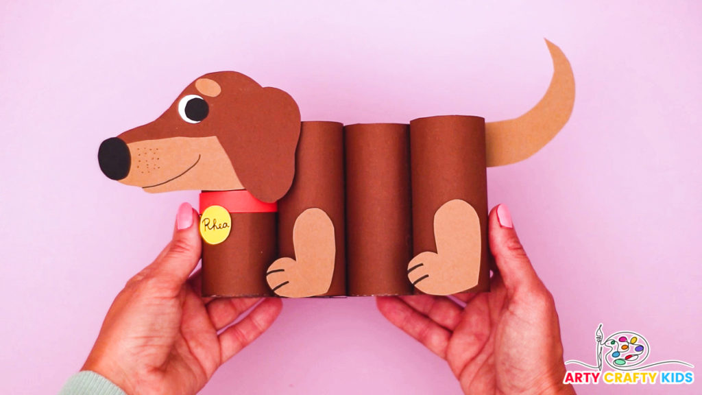 "An adorable DIY paper roll dog pencil holder made from recycled materials, perfect for organizing school supplies. The craft features a two-toned dachshund design with a cute collar and name tag. Suitable for kids of all ages with a printable template available