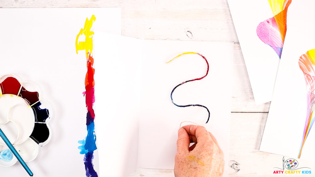 Step 3: Image of a hand placing the painted string onto a piece of thick paper.