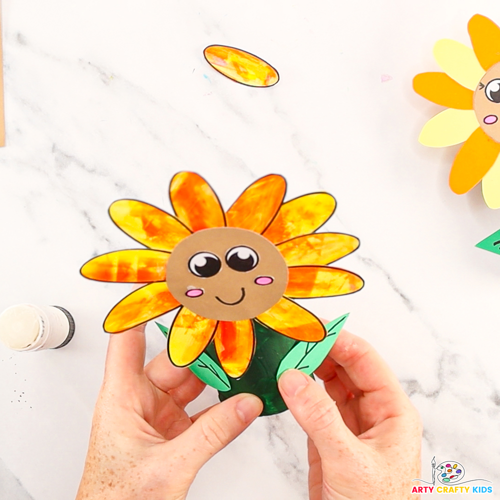 Image features a hand affixing the leaves onto the paper roll to complete the sunflower craft.