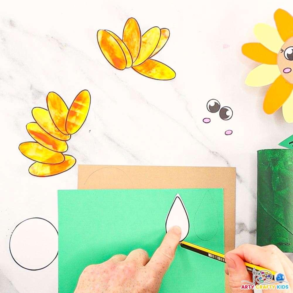 Image of a hand tracing the petals onto green paper. The sunflower petals, eyes and cheeks have been cut out.