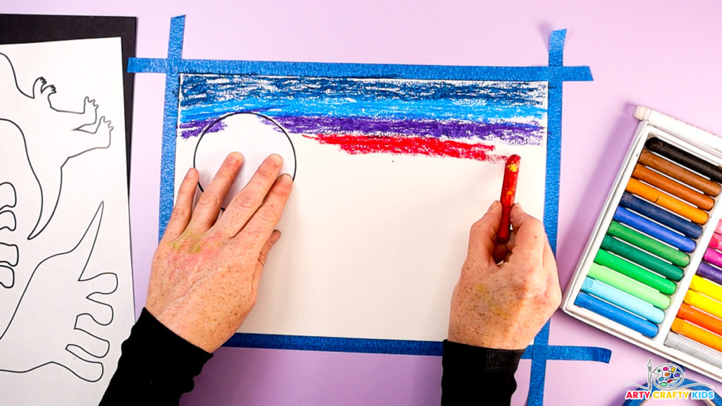 Image of a hand creating the sky, adding light blue, purple, and red oil pastel colors spread horizontally across the page. 