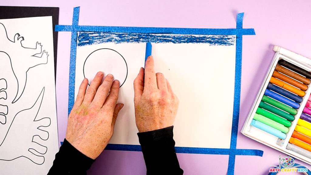 Image of a hand creating the sky, starting with a dark blue oil pastel spread horizontally across the page.