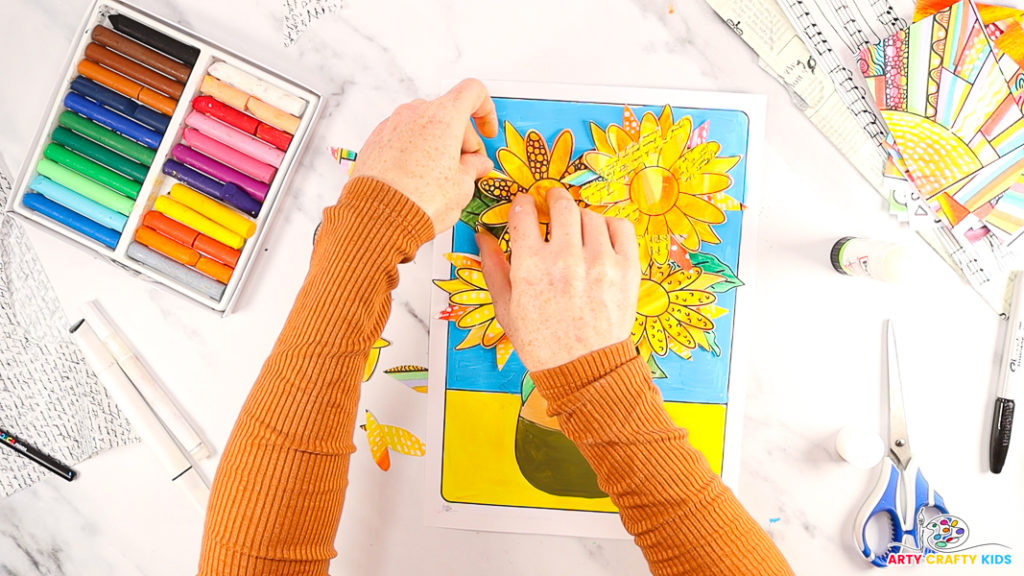 Image of a hand carefully glueing additional petals behind the base sunflowers to create a layered effect.