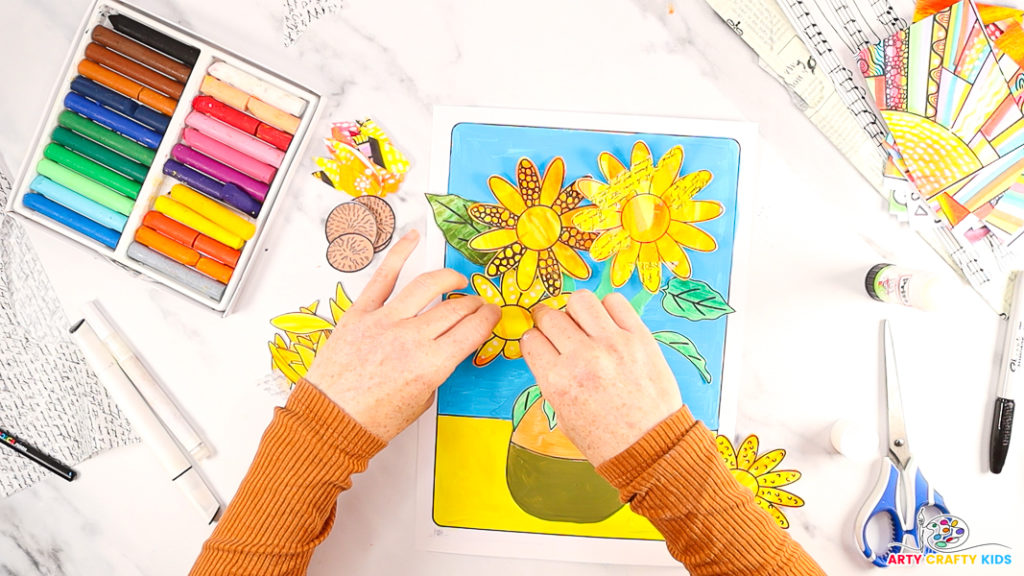 Image of a hand glueing the sunflower bases onto the template and gently lifting the petals to create a 3D effect.