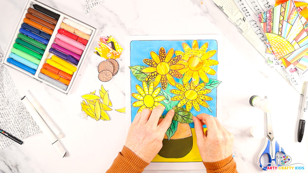 Image of a hand arranging the sunflowers and leaves onto the template. A hand is affixing the leaves to the stems.