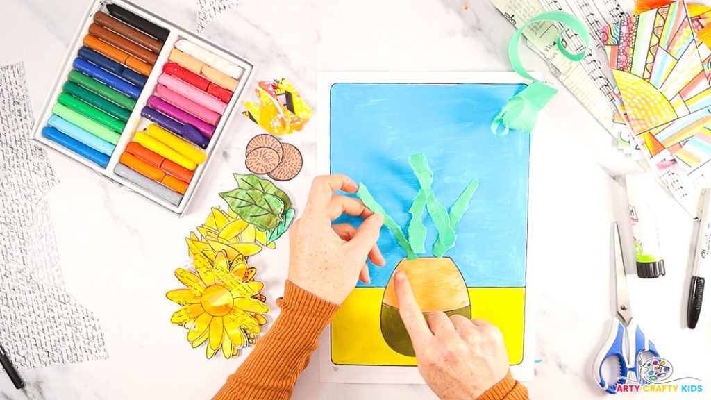 Image of a hand glueing the green paper stems above the vase on the backing template.