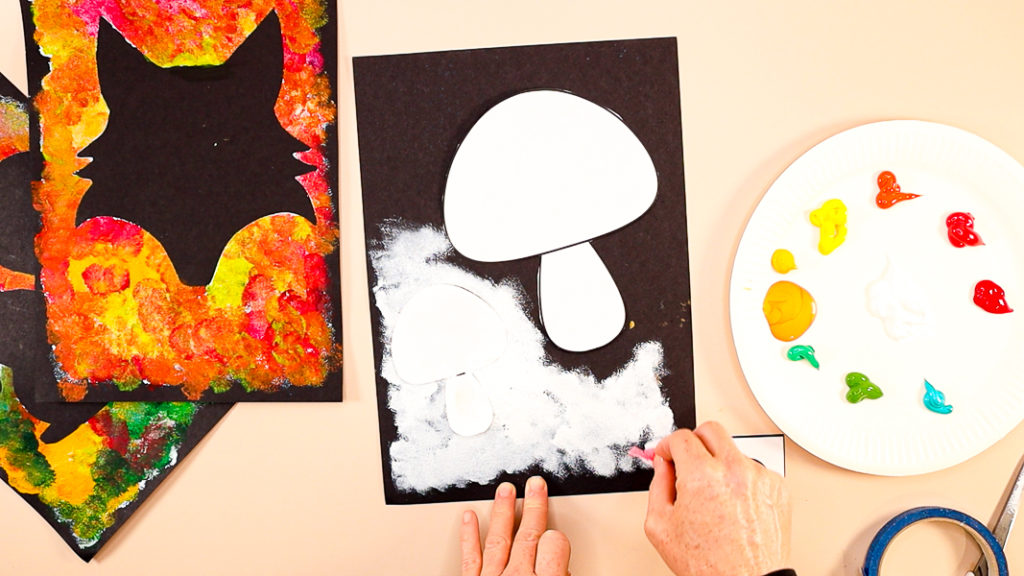 Image of a hand dabbing white paint around the mushroom silhouette templates.