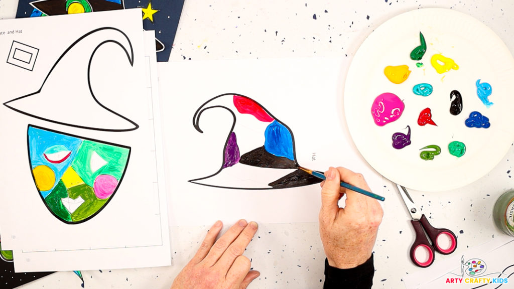 Image of a hand painting a segmented hat. Colors include red, blue, purple and black.