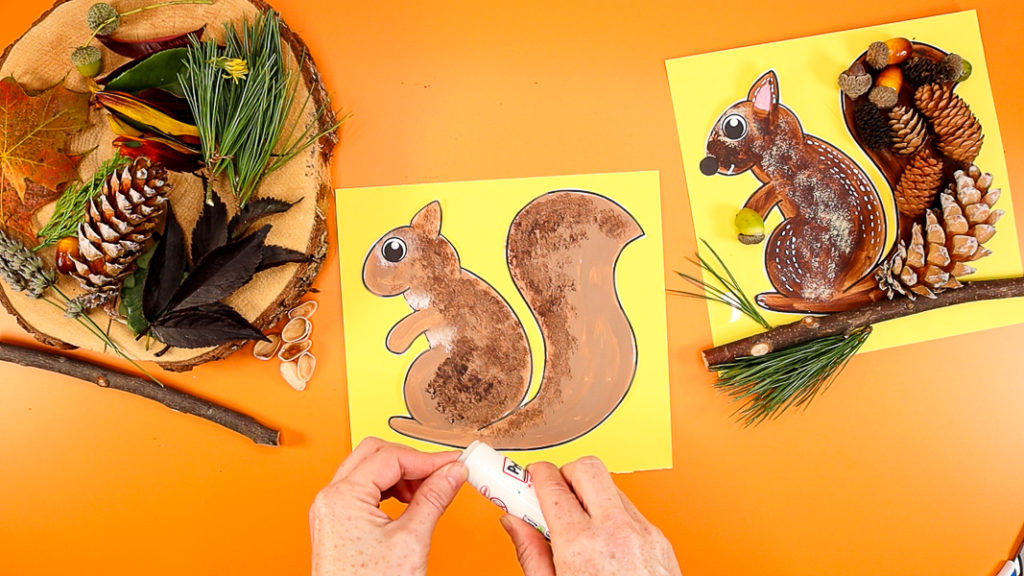 Image of a hand gluing the eye and nose onto the squirrel. The squirrel has also been affixed to a piece of colored cardstock.