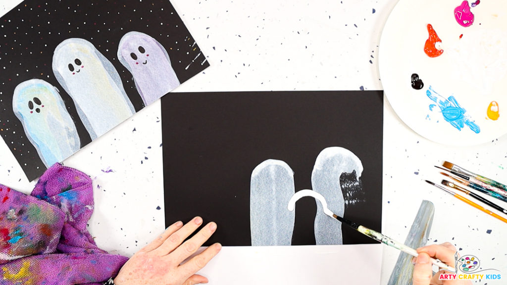 Image of a hand painting an arch between two squeegee painted ghosts.