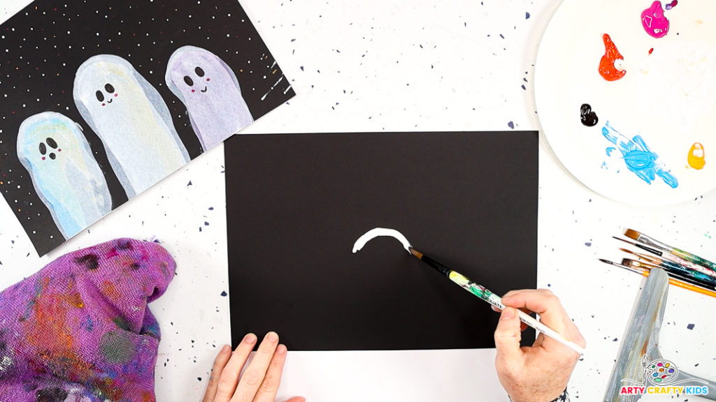 An image of a hand using a paintbrush to create a small white arch in the middle of a black sheet of card stock.