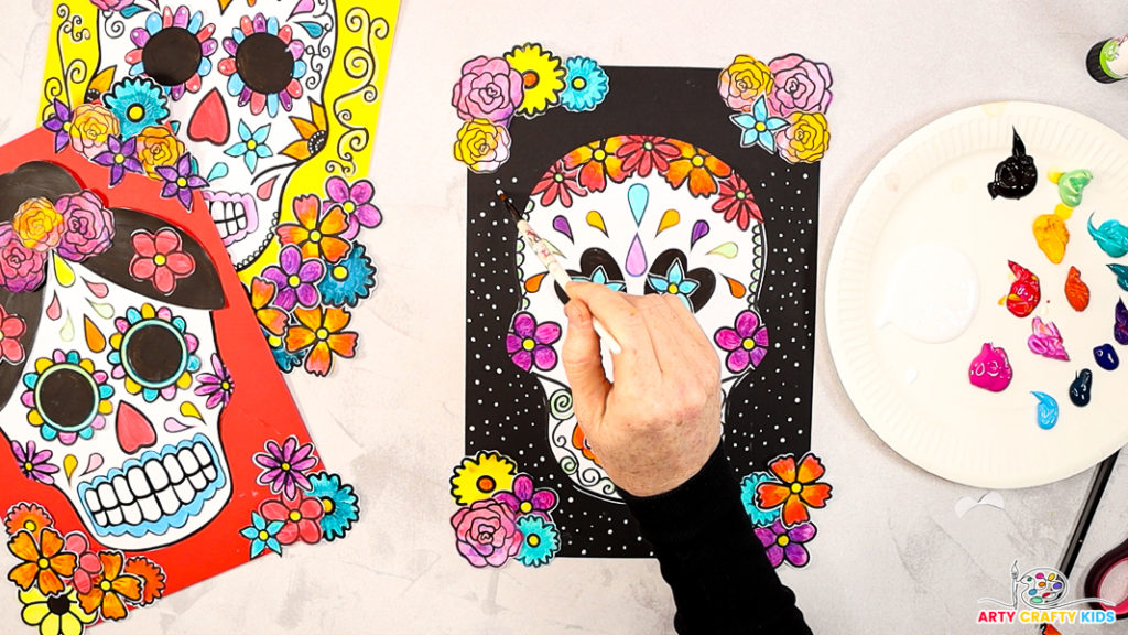 Image of a hand painting small white dots within the black space surrounding the sugar skull.