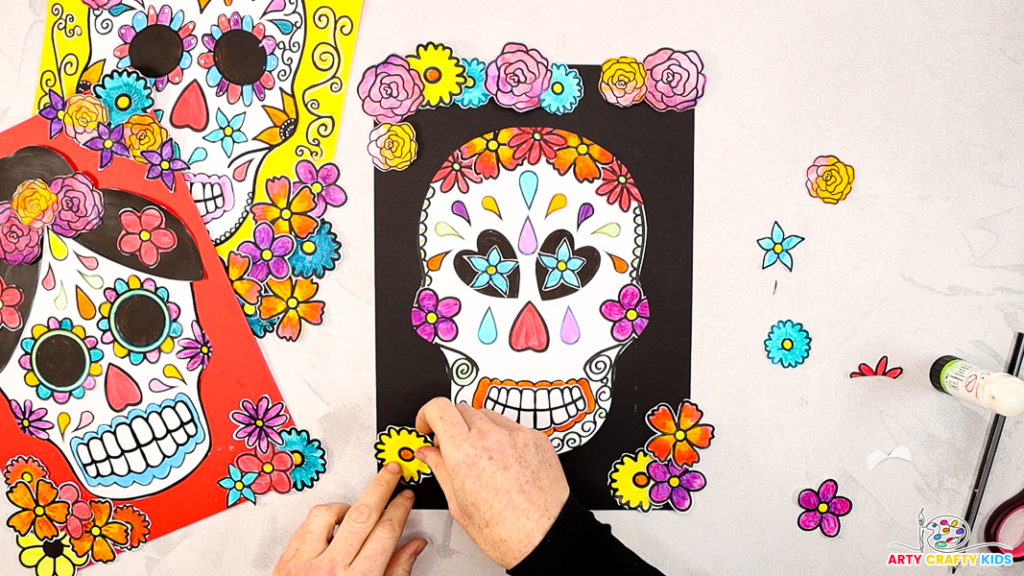 Image of hand glueing the remaining flowers around the sugar skull design.