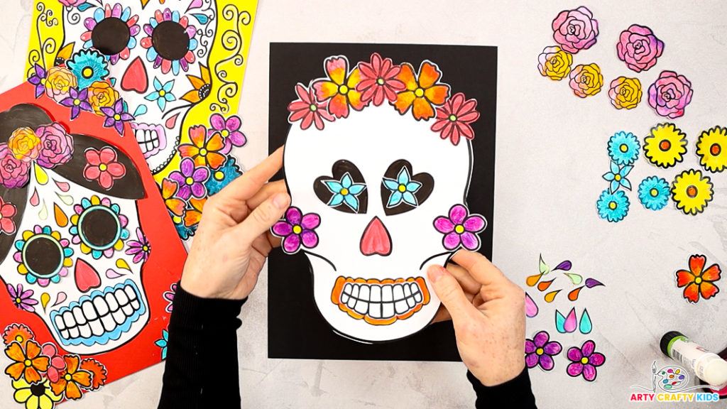 Image of a hand holding the sugar skull design with glued facial features and flowers positioned around the edges of the skull.