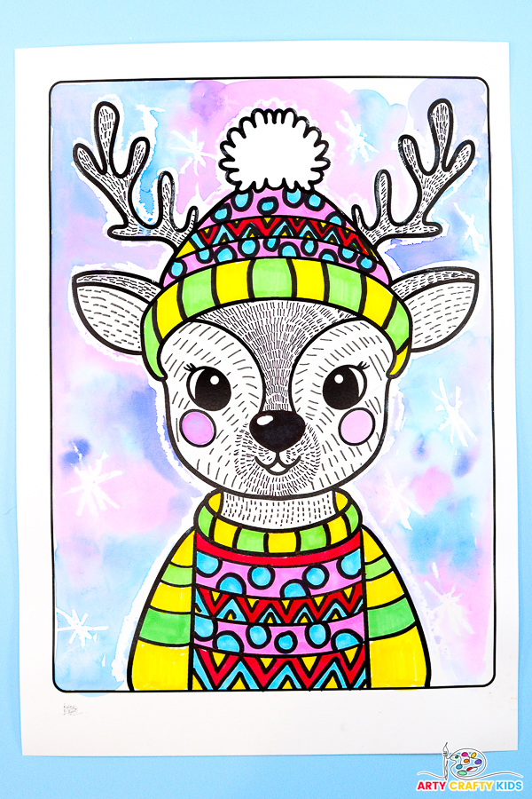 Illustrated reindeer line art project for kids featuring a festive design with a colorful Christmas sweater and bobble hat. The reindeer is surrounded by a wintery watercolor background with soft blue, purple, and pink hues, accented by wax-resist snowflakes.