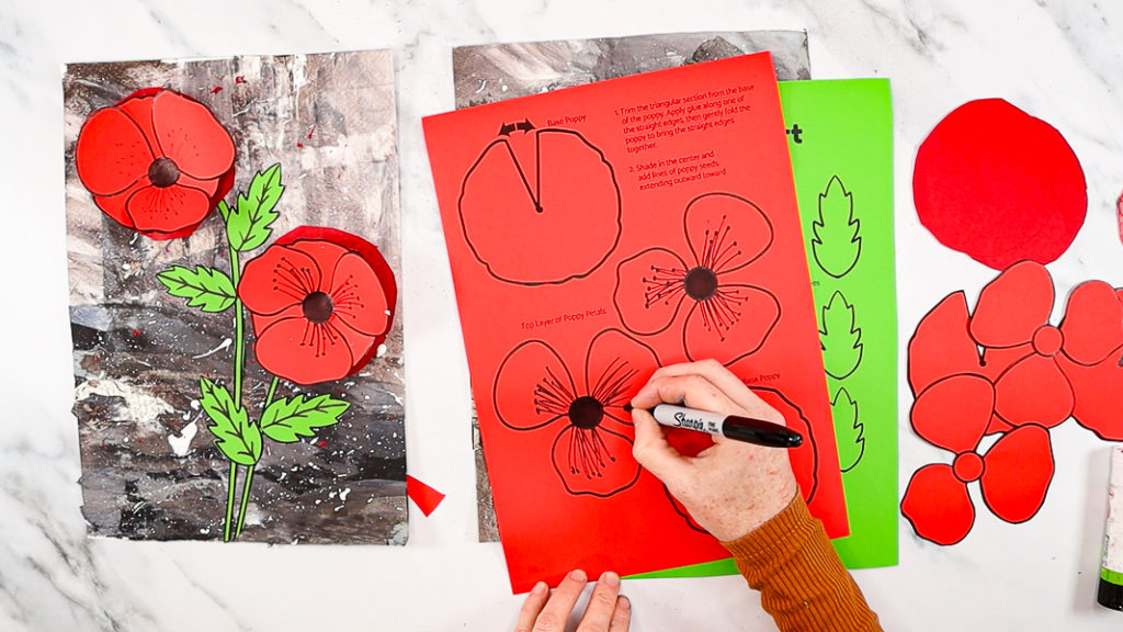 Image of a hand coloring in the center of the poppies with a black marker pen and drawing the seeds into the petals.