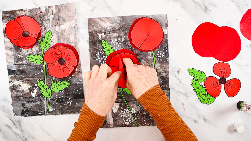 Image features a hand gluing the top layer of the poppy to complete the 3D poppy craft for remembrance day.