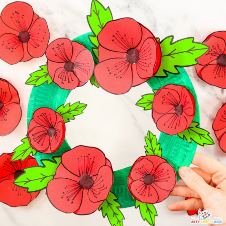 Paper plate poppy wreath craft for Remembrance Day, featuring vibrant red poppies and green leaves assembled on a circular paper plate base. A simple, meaningful craft project for kids to honor and remember.