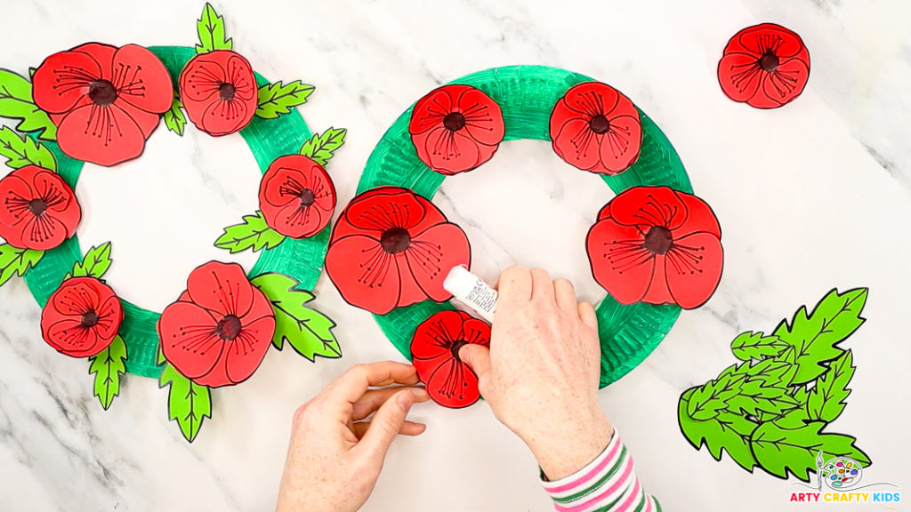 Image featuring a hand gluing the poppies onto the paper plate.