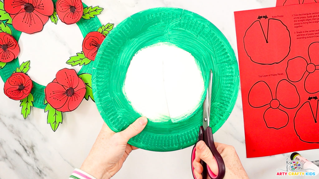 Image featuring a hand cutting out the center of a green painted paper plate.