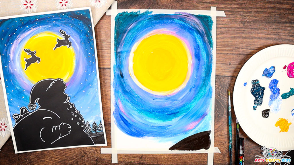 A step-by-step Christmas art project in progress, showing a vibrant painted night sky with shades of blue, pink, and purple swirling around a newly painted bright yellow moon.