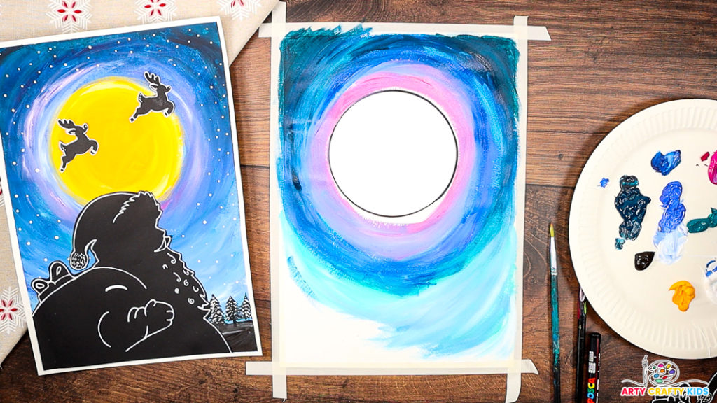 A step-by-step Christmas craft in progress, showing a partially painted night sky with layers of blue, pink, and purple swirling around a blank circular moon template. The completed Santa silhouette artwork is displayed on the left as inspiration, while a paint palette, brushes, and tools are arranged on the right, ready for use.