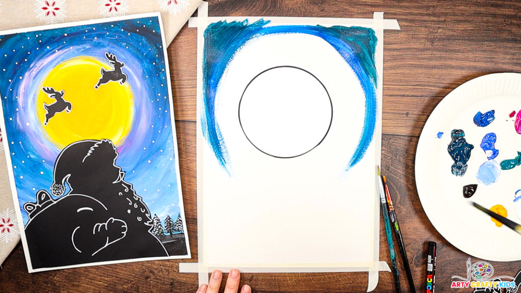 A step-by-step Christmas craft featuring a painted night sky in progress, with shades of blue swirling around a blank circular moon template. The completed Santa silhouette artwork is shown on the left as inspiration, while paints, brushes, and a palette with various colors are displayed on the right, ready for use.